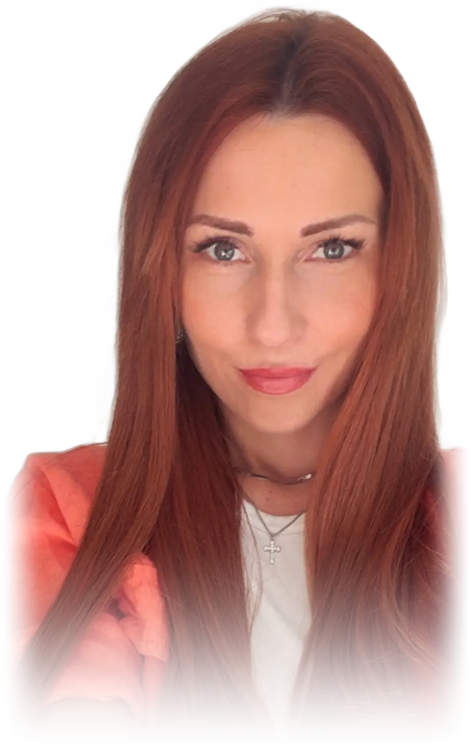 Milica, head and shoulders, long auburn hair, in a coral jacket over a white top with a fine chain and small cross at her neck, looking at the camera.